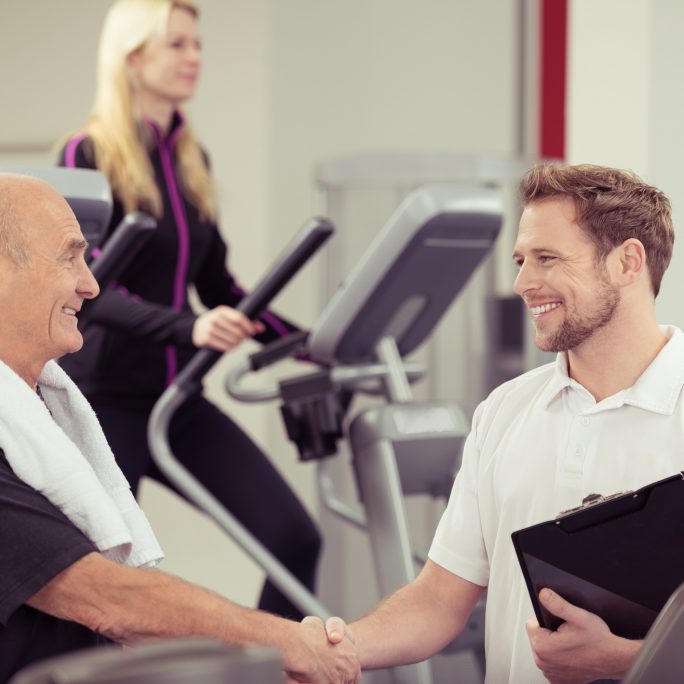 Close up Happy Old Man Shaking Hands with his Young Male Instructor at the Fitness Gym